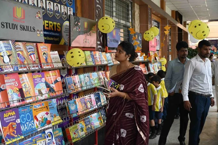 A visitor looking through the racks at the Sunbeam School Ballia book fair, a line of students filing past behind.