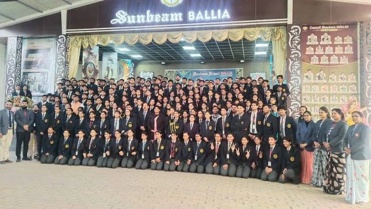 The youngest classes of Sunbeam School Ballia on stage in graduation caps and striped sashes, each holding a rolled certificate, with their teachers standing behind them.