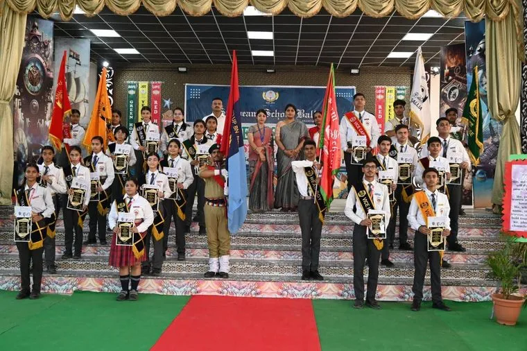 Students of Sunbeam School Ballia on stage holding framed certificates and the house flags, their sashes reading Head and Vice, with staff standing behind them.